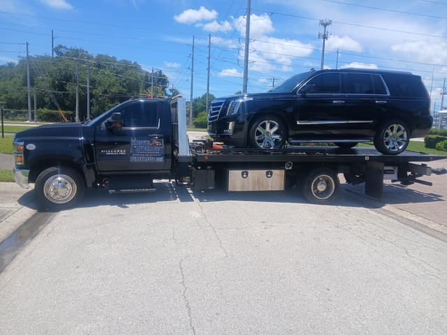 Black Cadillac Escalade with chrome wheels secured on the flatbed